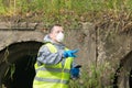 A man in a protective suit and mask with a phone in his hands shows his finger at the site of the epicenter of the environmental