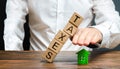 A man protects his hand with a figurine of a house from a falling tower of cubes with the word taxes. Heavy tax burden, protecting