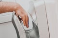 A man in a public place dries his hands in an electric dryer