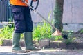 Man public worker cutting grass of the city street yard with trimmer machine with a smoke blow away