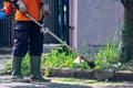 Man public worker cutting grass of the city street yard with trimmer machine with a smoke blow away