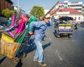 Man pulling a cart loaded with houswares crosses a busy street in Bangkok