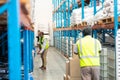 Man pulling pallet jack while supervisors work in aisle in warehouse. Royalty Free Stock Photo