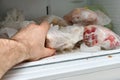 A man pulls frozen vegetables out of the freezer. A man takes corn from the fridge. Plastic containers with frozen meat,