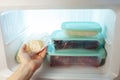 A man pulls frozen vegetables out of the freezer. A man takes corn from the fridge. Plastic containers with frozen meat,