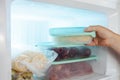 A man pulls frozen vegetables out of the freezer. A man takes corn from the fridge. Plastic containers with frozen meat,