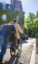 Man pushes bicycle with girl to the hill helping her ride up the street in Montmartre