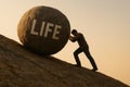 A man pushes a huge stone with the inscription LIFE. Royalty Free Stock Photo