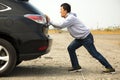 Man pushing a broken car down the rock road