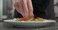 Man put cherry tomatoes on pesto fettuccine with mozzarella in pasta bowl on concrete countertop