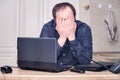 A man put hands to his face in the kitchen at home. Problems with overtime in the workplace at remote work from home Royalty Free Stock Photo