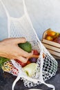 Man puts avocado to the eco string bag with fresh vegetables - tomatoes, purple potatoes, eggplants, carrots, sweet Royalty Free Stock Photo