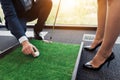 A man puts a golf ball in front of a business lady in a strict suit. A woman preparing for a blow