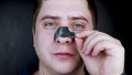 A man puts on and removes a strip for the nose from black dots. Coal cleaning strips from blackheads and comedones. The concept of