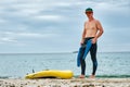 A man puts on a wetsuit on the beach and is going for a walk on the sea on a SUP board. Active recreation. Royalty Free Stock Photo