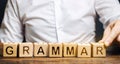 A man puts wooden blocks with the word Grammar. Set of structural rules governing the composition of clauses, phrases and words in