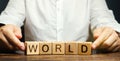 A man puts wooden blocks with the word World. The concept of globalization and global business. International relationships. Royalty Free Stock Photo