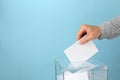 Man putting ballot into voting box on background