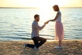 Man putting beautiful engagement ring on hand of his beloved near river