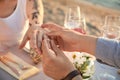 Man putting beautiful engagement ring on hand of his beloved outdoors, closeup