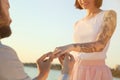 Man putting beautiful engagement ring on hand of his beloved outdoors