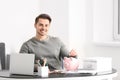 Man putting coin into piggy bank indoors. Money savings concept Royalty Free Stock Photo