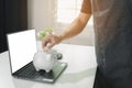 A man is putting a coin into a white piggy bank. In his office Royalty Free Stock Photo