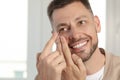 Man putting contact lens in his eye at home, space for text Royalty Free Stock Photo