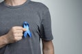 Man putting dark blue ribbon on his shirt. Awareness symbol