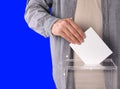 Man putting his vote into ballot box on blue background, closeup Royalty Free Stock Photo