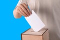 Man putting his vote into ballot box on light blue background, closeup Royalty Free Stock Photo