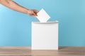 Man putting his vote into ballot box on light blue background, closeup Royalty Free Stock Photo