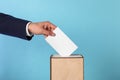 Man putting his vote into ballot box on light blue background, closeup Royalty Free Stock Photo