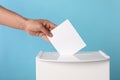 Man putting his vote into ballot box on light blue background, closeup Royalty Free Stock Photo