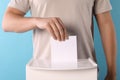 Man putting his vote into ballot box on light blue background, closeup Royalty Free Stock Photo