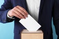 Man putting his vote into ballot box on light blue background, closeup Royalty Free Stock Photo