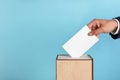 Man putting his vote into ballot box on light blue background, closeup. Space for text Royalty Free Stock Photo