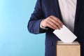 Man putting his vote into ballot box on light blue background, closeup. Space for text Royalty Free Stock Photo