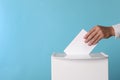 Man putting his vote into ballot box on light blue background, closeup. Space for text Royalty Free Stock Photo