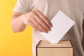 Man putting his vote into ballot box on yellow background, closeup