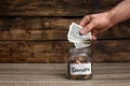 Man putting money into donation jar on table, closeup. Royalty Free Stock Photo