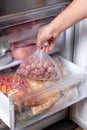 Man putting plastic bag with meatballs in refrigerator with frozen vegetables