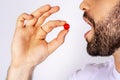 Man putting red pill in his mouth. Taking medications in motion. Man taking pills close up on white background Royalty Free Stock Photo