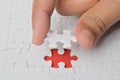 Man is putting a single part of a white puzzle in its place on the red background.