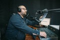 Man radio host or representer or journalist reads news from paper list in hand to studio microphone sitting at mixing sound panel