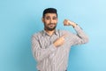 Man raising hands showing power, pointing at his biceps, feeling independent strong with proud look.