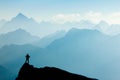 Man reaching summit after climbing and hiking enjoying freedom and looking towards mountains silhouettes panorama during