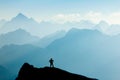 Man reaching summit after climbing and hiking enjoying freedom and looking towards mountains silhouettes panorama during