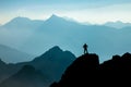 Man reaching summit after climbing and hiking enjoying freedom and looking towards mountains silhouettes panorama during