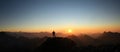 Man reaching summit enjoying freedom and looking towards mountains sunset. Royalty Free Stock Photo